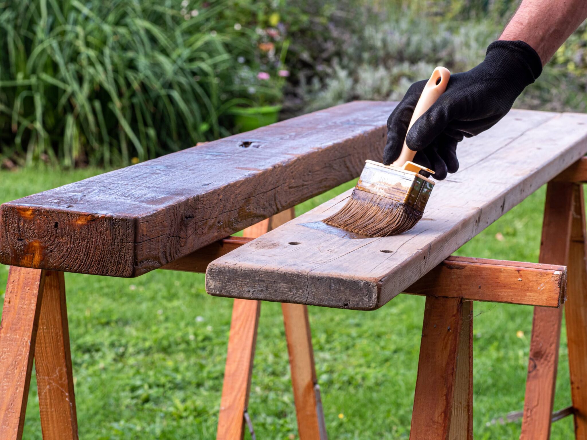 Im Garten streichen von 2 brettern auf zwei Holzböcken mit schwarzen Handschuh