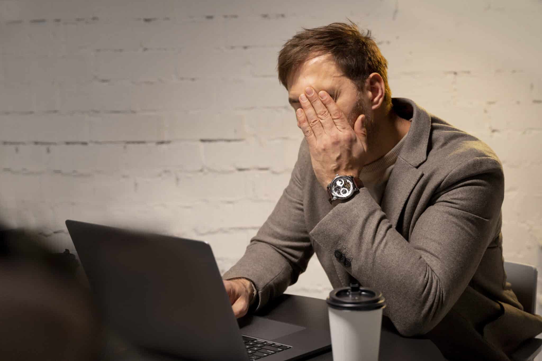 Büroangestellter im Stress: Ein Mann Mitte 30 sitzt erschöpft und überfordert vor seinem Laptop im Büro.