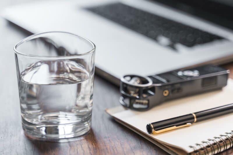 Glas Wasser neben Laptop auf Holztisch